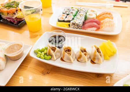 Tray of dumplings filled with meat, edamame beans, soy sauce and assorted sushi on wooden table Stock Photo