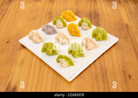 Cooked Chinese dumplings of different flavors on white plate on brown table Stock Photo