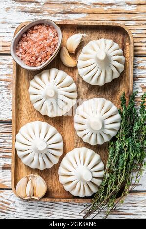 Frozen Raw dumplings Khinkali with beef and lamb meat on wooden tray with herbs. White wooden background. Top view Stock Photo