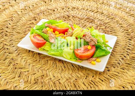 Mediterranean salad with large chunks of tomato, sweet corn, iceberg lettuce and canned northern bonito on white plate Stock Photo