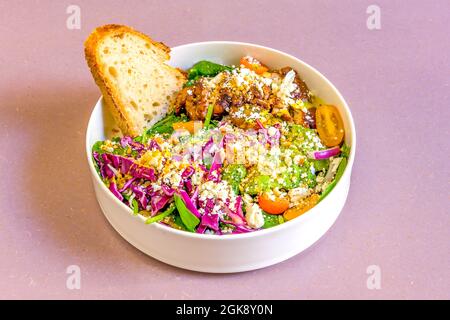 Nice white deep plate with purple cabbage salad, cherry tomatoes, grated cheese, roast chicken, spinach and a slice of rustic bread Stock Photo