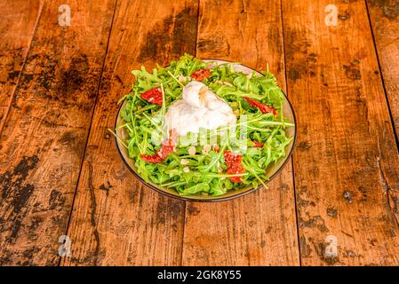 Arugula salad with raw almond slices, burrata cheese and dried tomatoes on reddish wood table Stock Photo