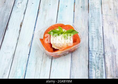 Fresh burrata cheese ball with tomato, pepper and basil slices inside a home delivery package on wooden background Stock Photo