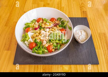 Popular cesar salad with sauce on the side in a white bowl, lamb's lettuce sprouts, roasted chicken pieces, fried croutons, lettuce and cherry tomatoe Stock Photo