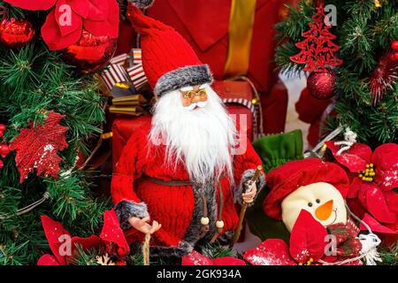 Bright colorful Santa Claus doll in red costume with long white beard on green fir tree branches background. Christmas and New Year holidays tradition Stock Photo