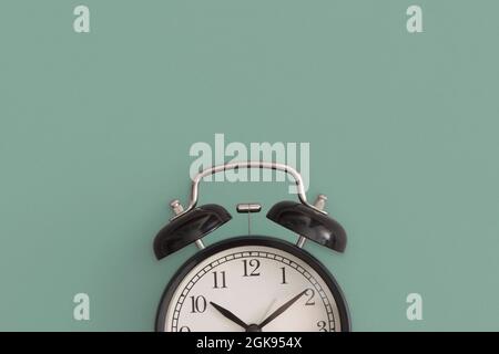 Black antique alarm clock on green background. Flat lay composition. Top view. Stock Photo