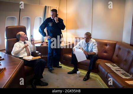 President Barack Obama reads a document between phone calls aboard Air Force One during the flight from Los Angeles, Calif. en route to Joint Base Andrews, Md., July 24, 2014. Brian McKeon, Executive Secretary and Chief of Staff of the National Security Council, left, talks with Donnie Gallion, lead CSO on Air Force One, as they  place a call for the President. (Official White House Photo by Pete Souza) This official White House photograph is being made available only for publication by news organizations and/or for personal use printing by the subject(s) of the photograph. The photograph may Stock Photo