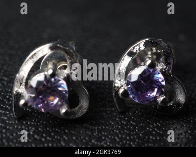 Close up shoot of silver earring with faceted amethyst gem. Shot on black background. Stock Photo
