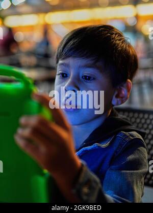 latino little boy in a bar playing concentrated a video game on a green tablet, vertical. Argentina Stock Photo