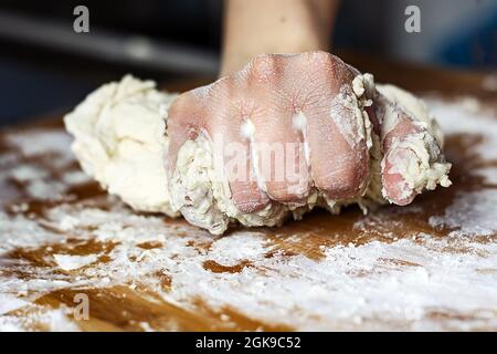 female hand kneading a flour dough by rolling it on a wooden board. Preparation of flour-based food such as bread or pizza Stock Photo