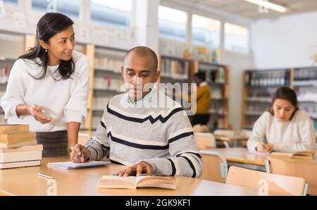 Female librarian helping hispanic student preparing to exam Stock Photo