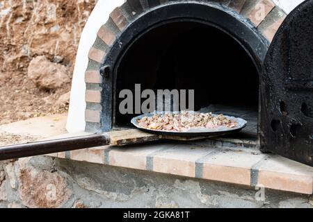 Man putting pizza in handmade white painted wood oven built outdoors with shovel Stock Photo