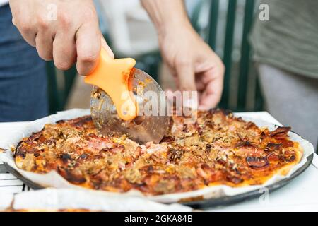 Man's hand cutting pizza made in artisan wood-fired oven built outdoors Stock Photo