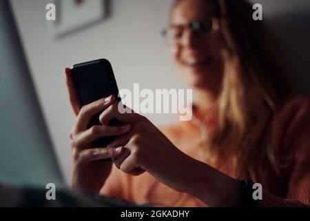 Closeup of young cheerful woman hands holding and using smartphone at home during quarantine and laughing Stock Photo