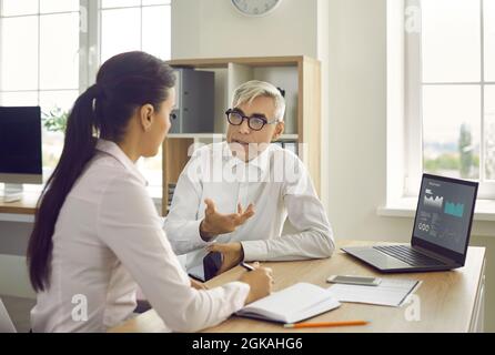 Two business people sitting at office desk with laptop and discussing work matters Stock Photo
