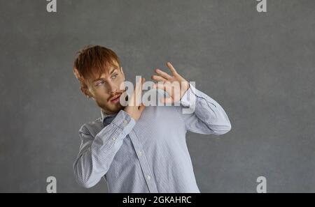 Afraid young casual man trying to protect himself with is arm standing over grey Stock Photo