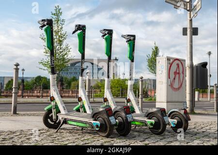 A row of four standing electric escooters or e-scooters from the company LIME on the sidewalk in Berlin Stock Photo