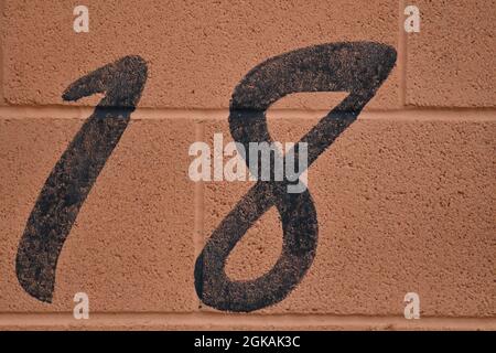 A black number 18, eighteen painted in black on an orange breeze block wall outside a racing car garage entrance Stock Photo