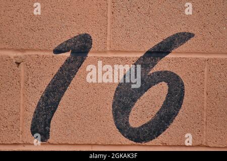 A black number 16, sixteen, painted in black on an orange breeze block wall outside a racing car garage entrance Stock Photo