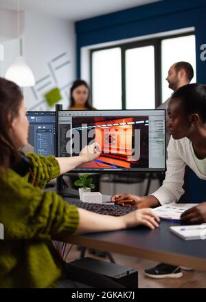 Diverse women game developers creating game interface sitting in startup creative production company pointing at pc displays. Workers developing online graphics video games with modern technology Stock Photo