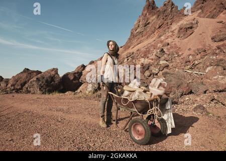 Young female worker standing with wheelbarrow in the desert and mining Stock Photo