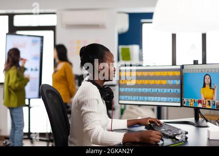 Black retoucher artist analysing images on pc with two monitors and retouching digital assets with stylus pencil. African designer using photo editing software working in creative production office Stock Photo