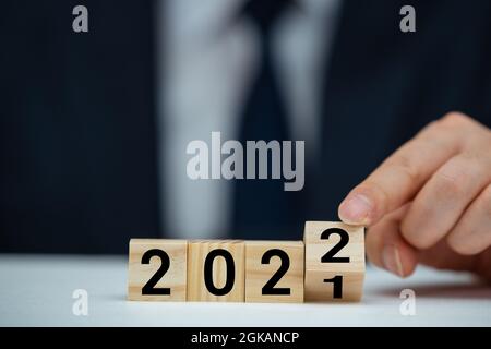 Businessman hand holding wooden cube with flip over block 2021 to 2022 text on table background. Stock Photo