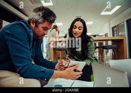 Caucasian male worker helping businesswoman understand ideas using digital tablet during lunch break relaxing in lounge  Stock Photo