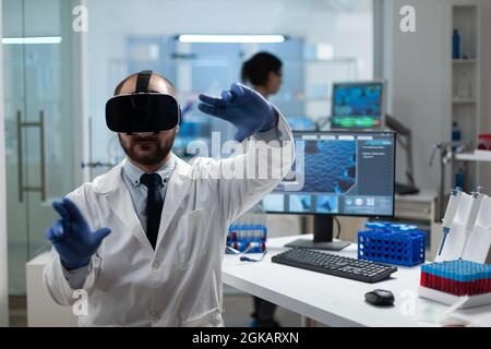 Chemist researcher analyzing sickness development using virtual reality headset during medical experiment in biochemistry hospital laboratory. Modern biotechnology equipment Stock Photo