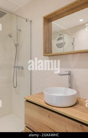 Modern bathroom with shower, round white sink, wooden base and mirror frame. Minimalist style interior design in warm colors. Stock Photo