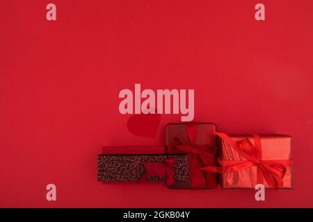 Top view composition of various Christmas presents wrapped in paper with ribbons and decorative balls placed on bright red surface with empty space Stock Photo