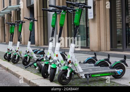 A row of six standing and one lying electric escooters or e-scooters from the company LIME on the sidewalk in Berlin Stock Photo