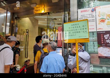 Shanghai, Shanghai, China. 14th Sep, 2021. On September 14, 2021, Shanghai, the storm brought by Typhoon ''Chanthu'' is still going on, but at the door of the main store in ''Guangming Village'' on Huaihai Middle Road, there are still many citizens waiting in the rain to buy fresh meat mooncakes. Citizens in line on Huaihai Middle Road stretched to the intersection of Chengdu South Road on the side. Some citizens also sat on the sidewalk with small stools and waited. Credit: ZUMA Press, Inc./Alamy Live News Stock Photo