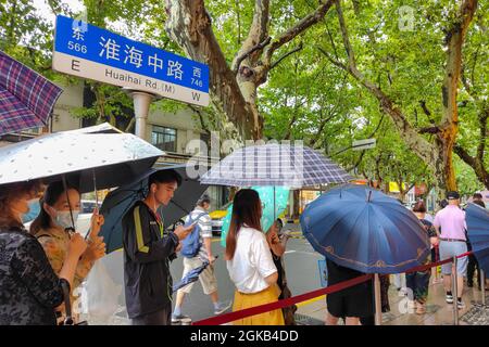 Shanghai, Shanghai, China. 14th Sep, 2021. On September 14, 2021, Shanghai, the storm brought by Typhoon ''Chanthu'' is still going on, but at the door of the main store in ''Guangming Village'' on Huaihai Middle Road, there are still many citizens waiting in the rain to buy fresh meat mooncakes. Citizens in line on Huaihai Middle Road stretched to the intersection of Chengdu South Road on the side. Some citizens also sat on the sidewalk with small stools and waited. Credit: ZUMA Press, Inc./Alamy Live News Stock Photo