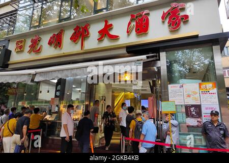 Shanghai, Shanghai, China. 14th Sep, 2021. On September 14, 2021, Shanghai, the storm brought by Typhoon ''Chanthu'' is still going on, but at the door of the main store in ''Guangming Village'' on Huaihai Middle Road, there are still many citizens waiting in the rain to buy fresh meat mooncakes. Citizens in line on Huaihai Middle Road stretched to the intersection of Chengdu South Road on the side. Some citizens also sat on the sidewalk with small stools and waited. Credit: ZUMA Press, Inc./Alamy Live News Stock Photo