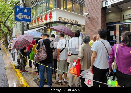 Shanghai, Shanghai, China. 14th Sep, 2021. On September 14, 2021, Shanghai, the storm brought by Typhoon ''Chanthu'' is still going on, but at the door of the main store in ''Guangming Village'' on Huaihai Middle Road, there are still many citizens waiting in the rain to buy fresh meat mooncakes. Citizens in line on Huaihai Middle Road stretched to the intersection of Chengdu South Road on the side. Some citizens also sat on the sidewalk with small stools and waited. Credit: ZUMA Press, Inc./Alamy Live News Stock Photo