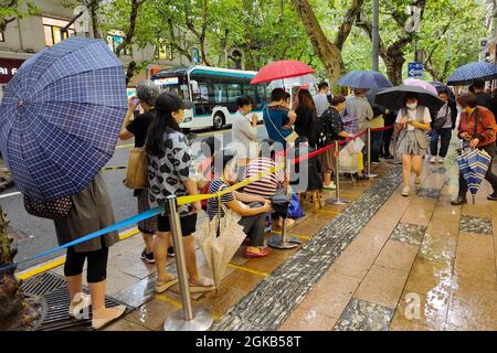 Shanghai, Shanghai, China. 14th Sep, 2021. On September 14, 2021, Shanghai, the storm brought by Typhoon ''Chanthu'' is still going on, but at the door of the main store in ''Guangming Village'' on Huaihai Middle Road, there are still many citizens waiting in the rain to buy fresh meat mooncakes. Citizens in line on Huaihai Middle Road stretched to the intersection of Chengdu South Road on the side. Some citizens also sat on the sidewalk with small stools and waited. Credit: ZUMA Press, Inc./Alamy Live News Stock Photo