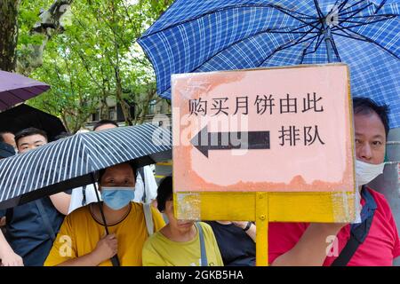 Shanghai, Shanghai, China. 14th Sep, 2021. On September 14, 2021, Shanghai, the storm brought by Typhoon ''Chanthu'' is still going on, but at the door of the main store in ''Guangming Village'' on Huaihai Middle Road, there are still many citizens waiting in the rain to buy fresh meat mooncakes. Citizens in line on Huaihai Middle Road stretched to the intersection of Chengdu South Road on the side. Some citizens also sat on the sidewalk with small stools and waited. Credit: ZUMA Press, Inc./Alamy Live News Stock Photo