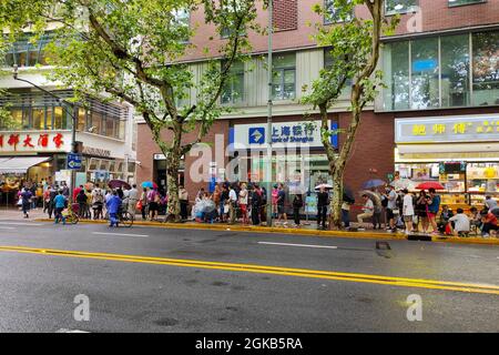 Shanghai, Shanghai, China. 14th Sep, 2021. On September 14, 2021, Shanghai, the storm brought by Typhoon ''Chanthu'' is still going on, but at the door of the main store in ''Guangming Village'' on Huaihai Middle Road, there are still many citizens waiting in the rain to buy fresh meat mooncakes. Citizens in line on Huaihai Middle Road stretched to the intersection of Chengdu South Road on the side. Some citizens also sat on the sidewalk with small stools and waited. Credit: ZUMA Press, Inc./Alamy Live News Stock Photo