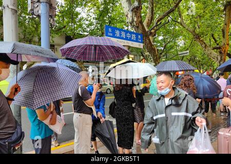 Shanghai, Shanghai, China. 14th Sep, 2021. On September 14, 2021, Shanghai, the storm brought by Typhoon ''Chanthu'' is still going on, but at the door of the main store in ''Guangming Village'' on Huaihai Middle Road, there are still many citizens waiting in the rain to buy fresh meat mooncakes. Citizens in line on Huaihai Middle Road stretched to the intersection of Chengdu South Road on the side. Some citizens also sat on the sidewalk with small stools and waited. Credit: ZUMA Press, Inc./Alamy Live News Stock Photo