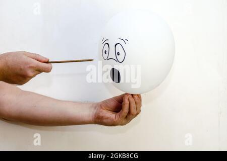 A balloon with a face painted on it and a rusty nail. Man holdin Stock Photo