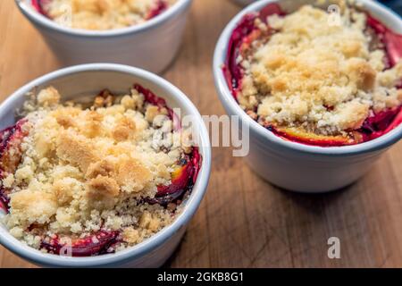 Sweet dessert made of plums and crumbles in small, white bowls on a woodem plank. Delicious food. Stock Photo