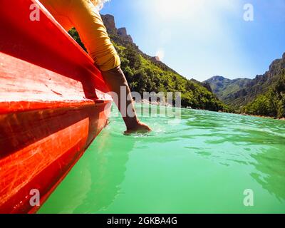 Woman traveler enjoying her kayak ride on canyon with hand dipping underwater and mountain in the background. Woman dipping her hands in lake water wh Stock Photo
