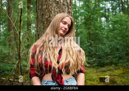 Beautiful blonde girl leaning on the tree with her eyes closed. Stock Photo