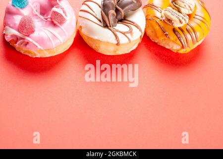 Photo of 3 donuts decorated with cookies and gumdrop on a red background.The donuts are dipped in strawberry chocolate, dark chocolate and white choco Stock Photo