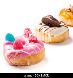 Close-up of a pink donuts decorated with jelly beans and two out-of-focus donuts in the background.The photo is taken in square format on a white back Stock Photo