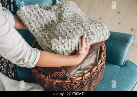 Women's hands fold a stack of warm knitted sweaters in wicker b Stock Photo