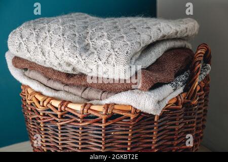 Stack of knitted sweaters on wicker basket. Stock Photo
