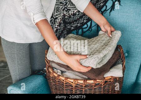 Women's hands fold a stack of warm knitted sweaters in wicker b Stock Photo