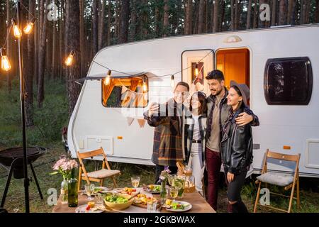 Group of happy young friends making selfie by mobile house while enjoying rest in the forest Stock Photo